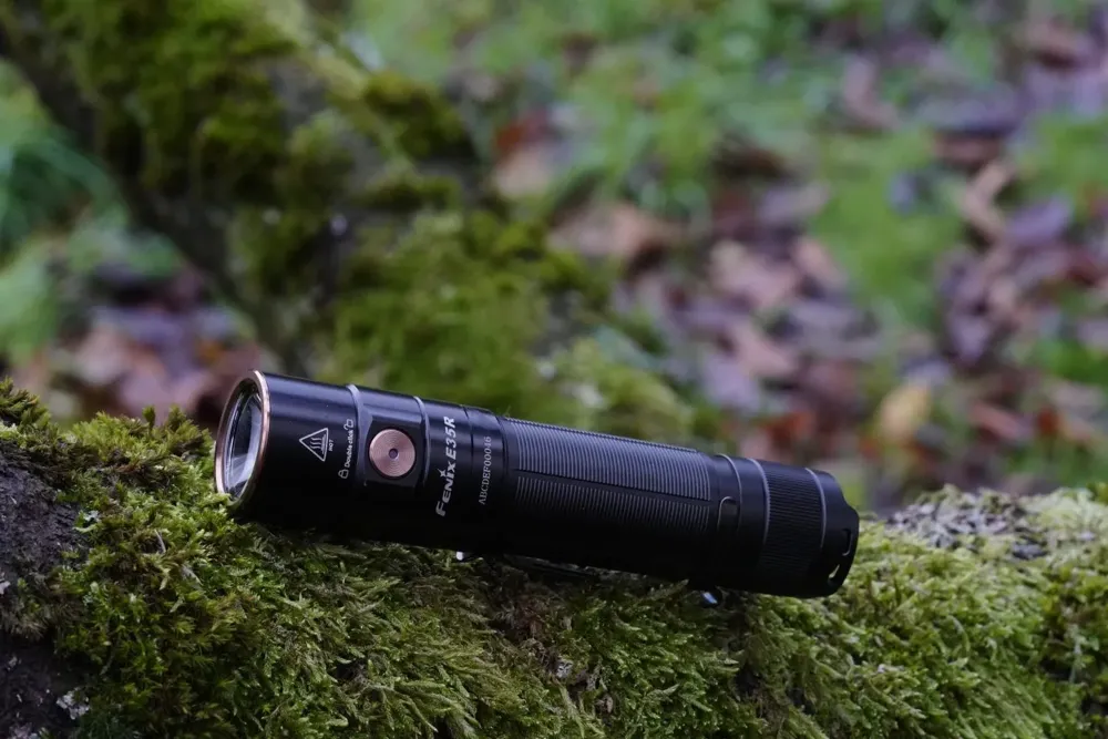 Linterna Fenix color negro sobre un tronco con musgo