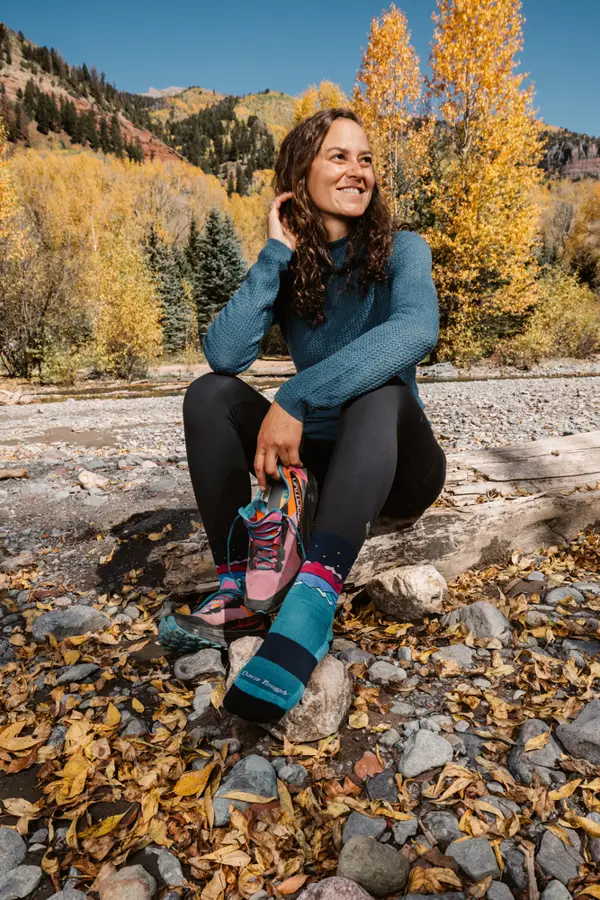 Chica con mallas negras sentada sobre piedra al fondo árboles con hojas amarillas
