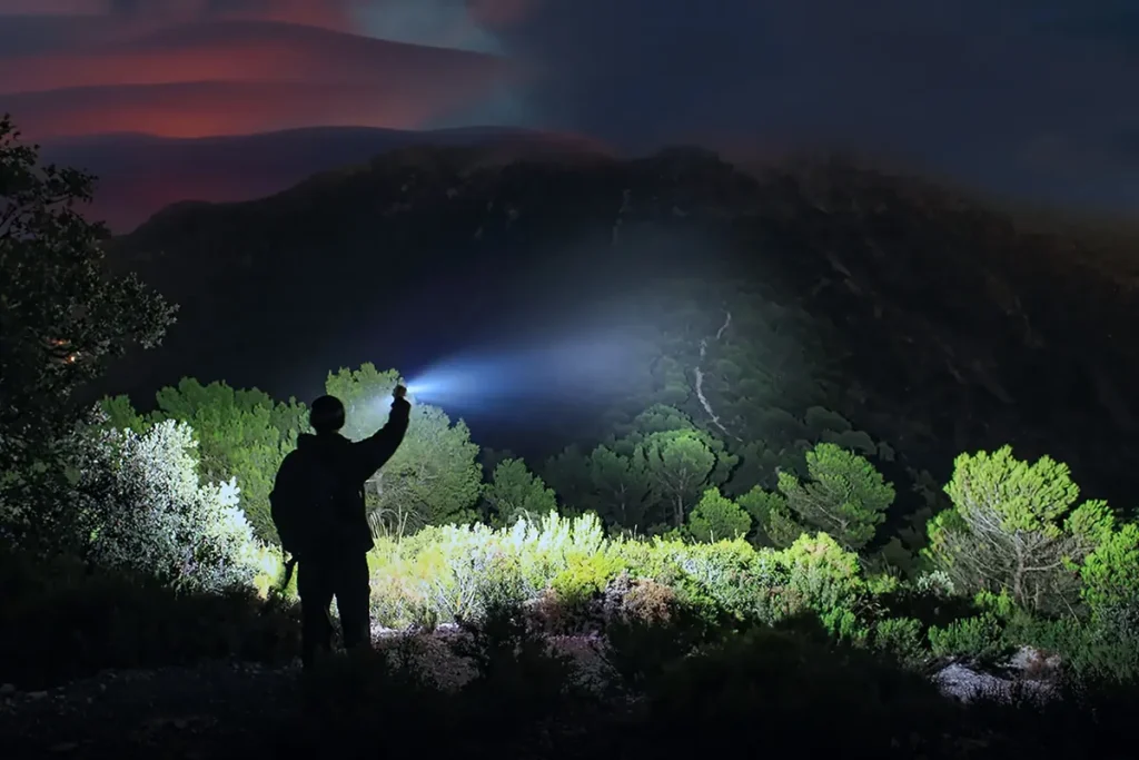 Fenixlight. Senderista en la montaña de noche iluminando el bosque con una linterna Fenixlight