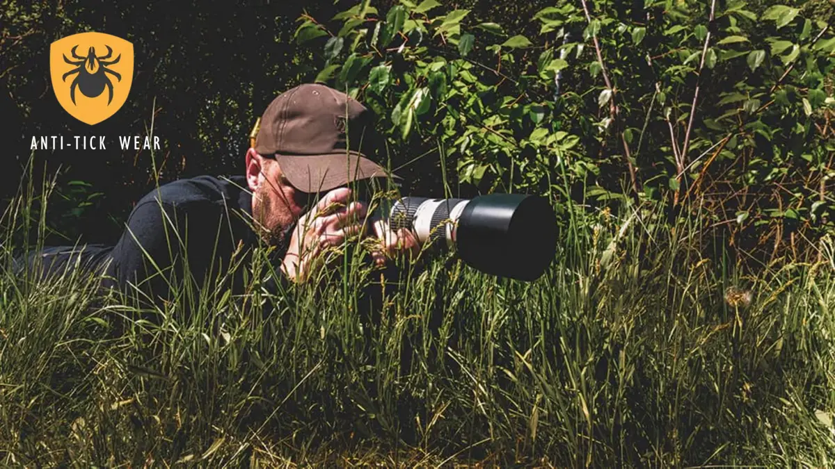 Un chico y una chica en un bosque, el chico lleva un rifle y apunta con el dedo y la chica lleva unos prismáticos mirando al horizonte.