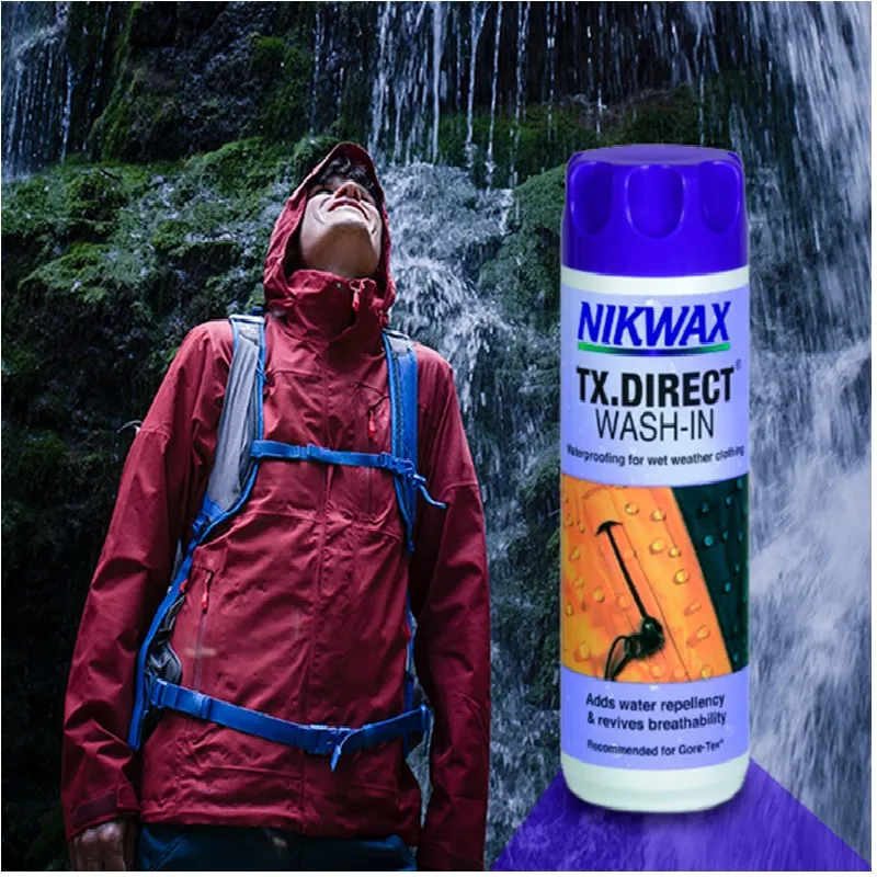 Chico con chaqueta burdeos con una cascada detrás y al lado un bote morado nikwax 