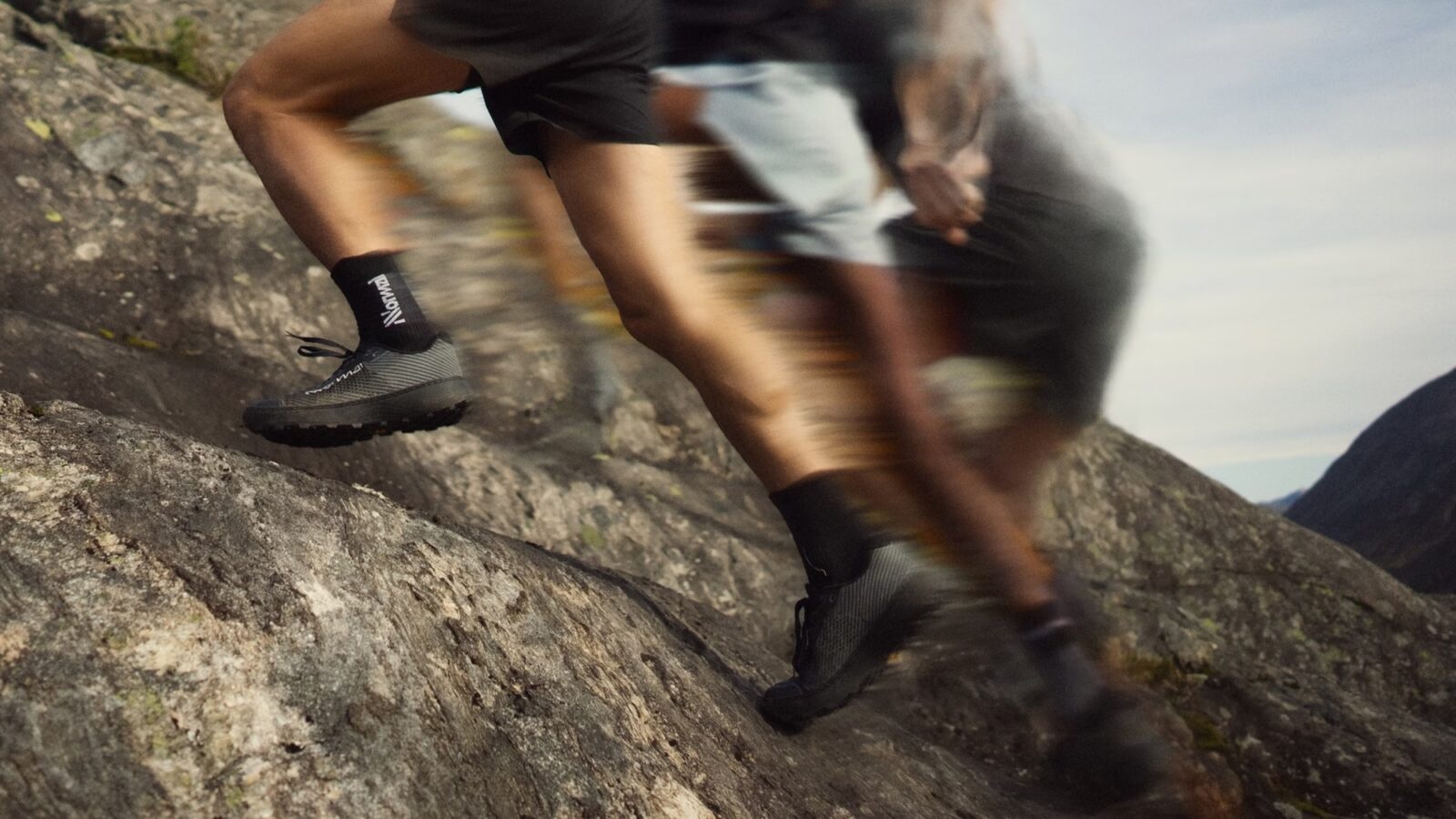 Corredor trepando por una roca con pantalones negros cortos así como los calcetines y las zapatillas Nnormal