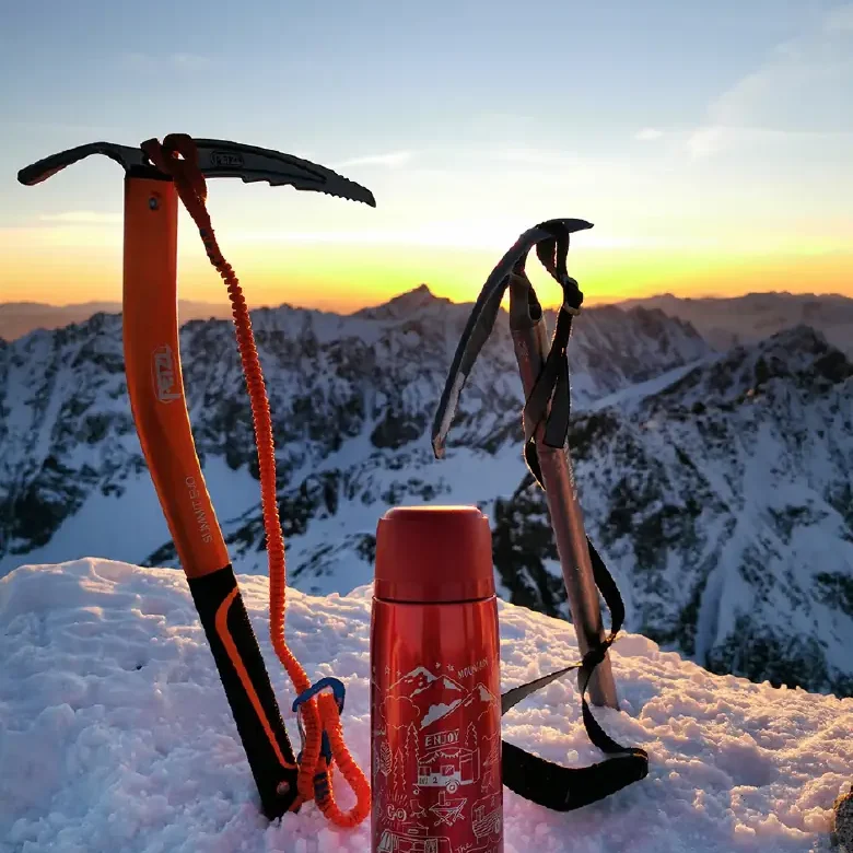 Montaña nevada con dos piolets rojos y botella Zojirushi roja